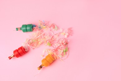 Beautiful serpentine bursting out of small party poppers on pink background, flat lay. Space for text