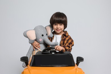 Photo of Cute little boy with toy elephant driving children's car on grey background
