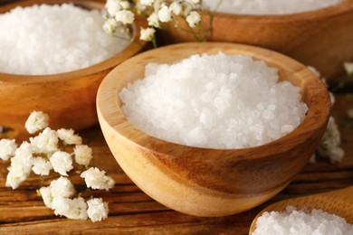 Aromatic sea salt and beautiful flowers on wooden table, closeup