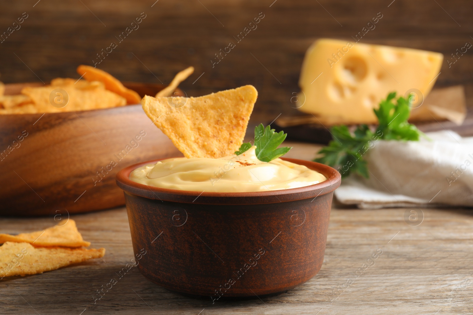 Photo of Delicious cheese sauce with nacho and parsley on wooden table, closeup