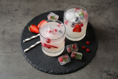 Glasses of refreshing drink with ice cubes and berries on grey table