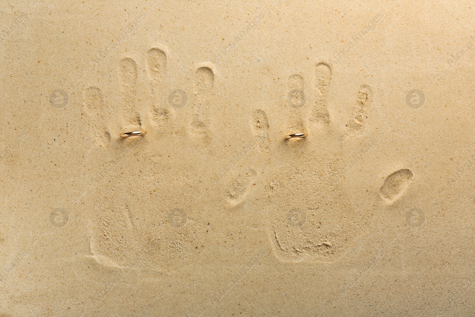 Photo of Honeymoon concept. Handprints and two golden rings on sand, top view