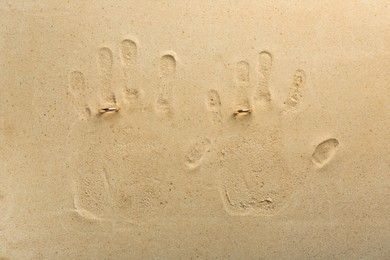 Honeymoon concept. Handprints and two golden rings on sand, top view