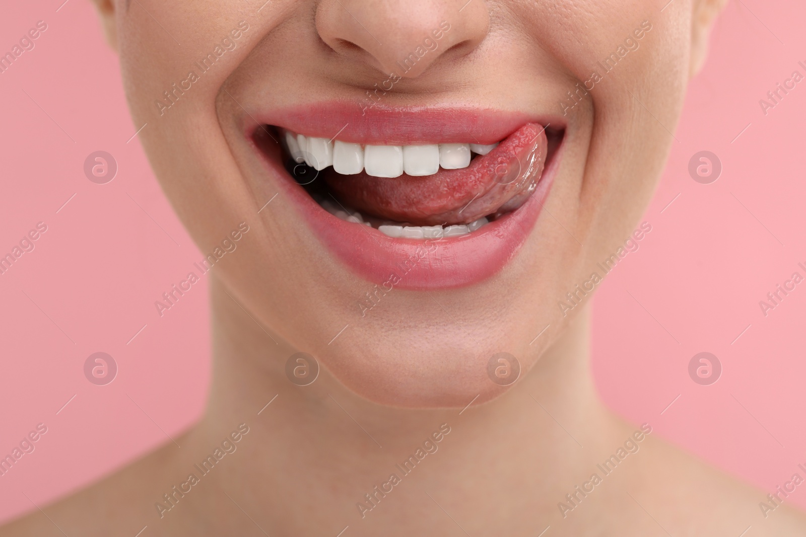 Photo of Young woman licking her teeth on pink background, closeup