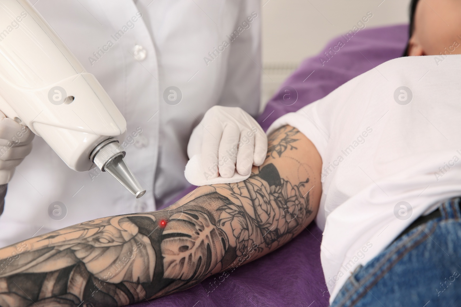 Photo of Young woman undergoing laser tattoo removal procedure in salon, closeup