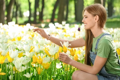 Photo of Beautiful young woman near blossoming tulips in green park on sunny spring day