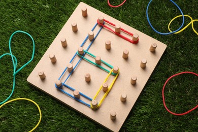 Photo of Wooden geoboard with number 6 made of rubber bands on artificial grass, above view. Educational toy for motor skills development