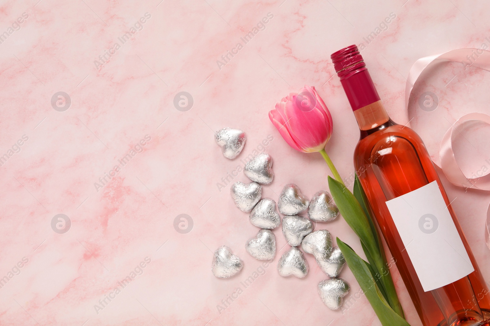 Photo of Delicious heart shaped chocolate candies, beautiful tulip and bottle of wine on pink table, flat lay. Space for text