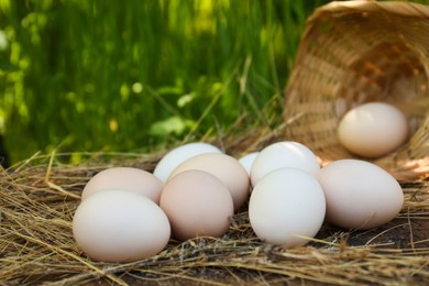 Photo of Fresh raw eggs and straw on wooden surface outdoors, closeup