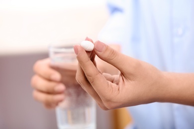 Photo of Woman holding pill and glass of water on blurred background, closeup. Space for text