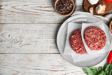 Flat lay composition with raw meat cutlets for burger on white wooden table. Space for text