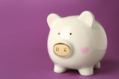 Photo of Ceramic piggy bank on purple background. Space for text