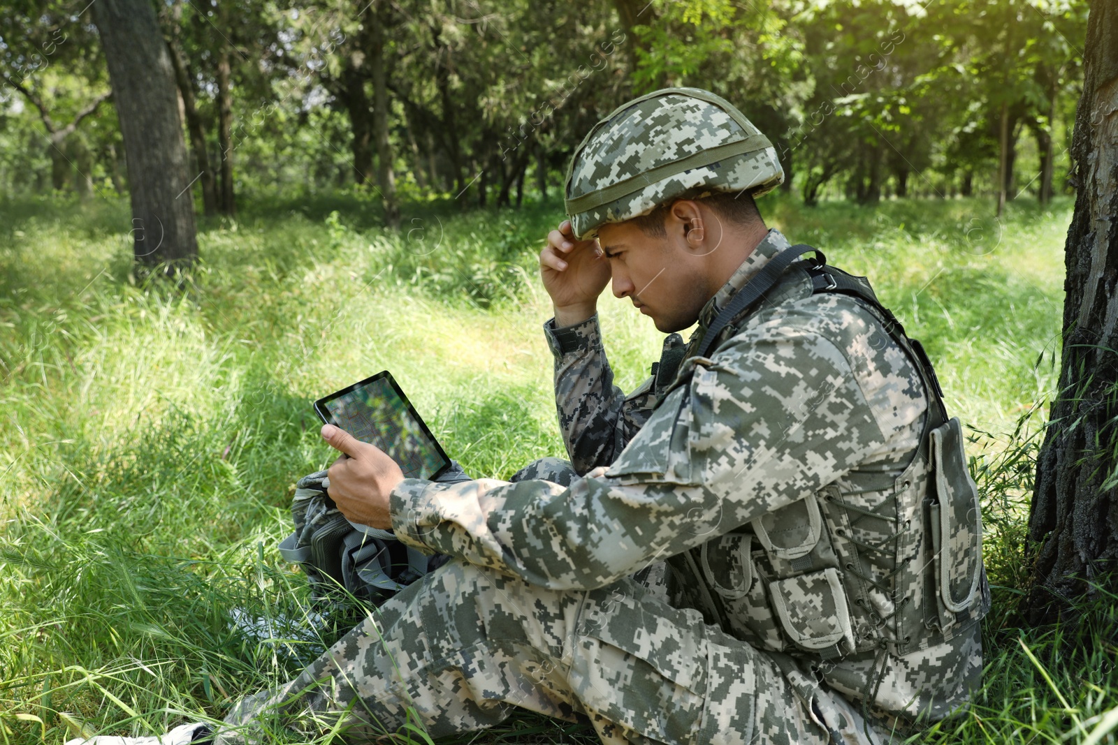 Photo of Soldier with backpack using tablet near tree in forest