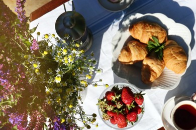 Photo of Beautiful bouquet of wildflowers, ripe strawberries, tea and croissants on table outdoors, flat lay