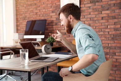 Photo of Young man using video chat on laptop in home office. Space for text