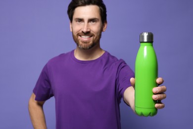 Photo of Man with green thermo bottle against violet background. Focus on hand