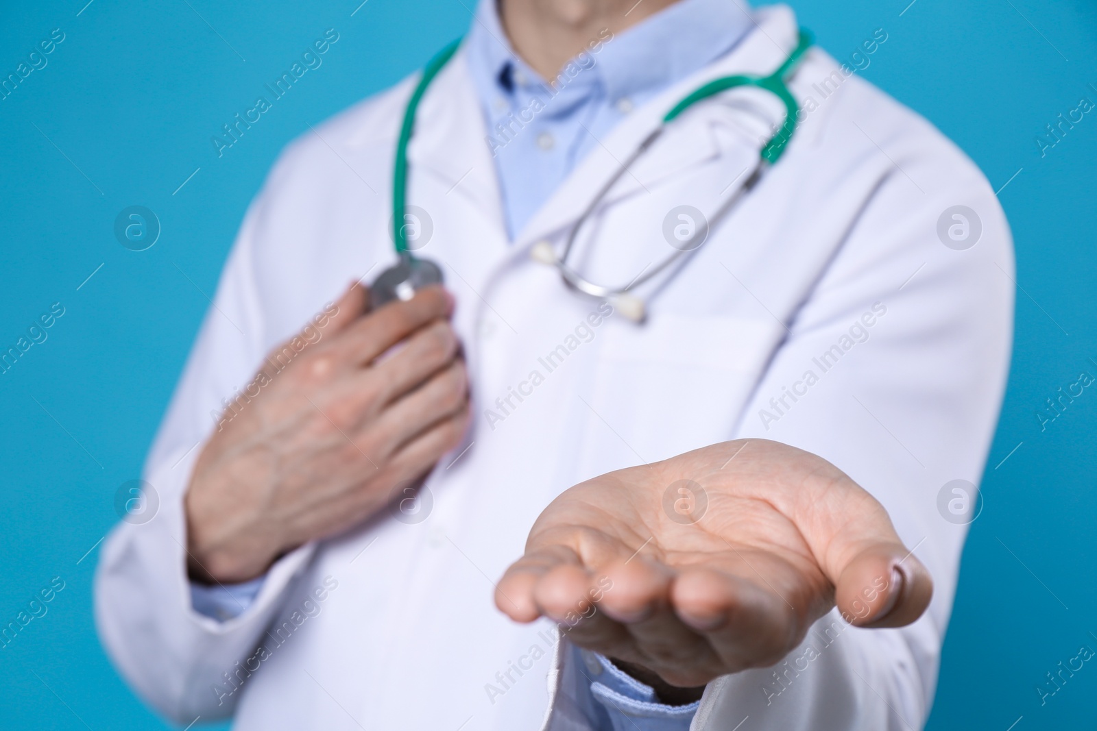 Photo of Doctor with stethoscope holding something on light blue background, closeup. Cardiology concept