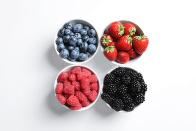 Bowls with raspberries and different berries on white background