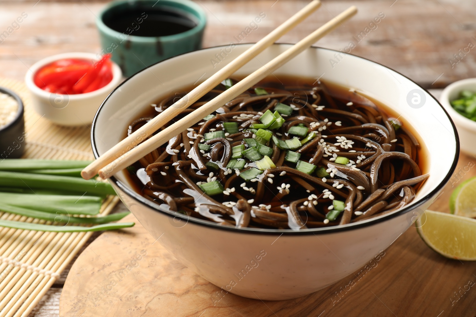 Photo of Tasty soup with buckwheat noodles (soba), onion in bowl and chopsticks on table, closeup