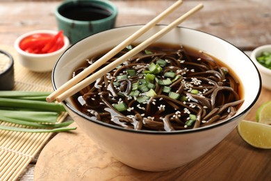 Photo of Tasty soup with buckwheat noodles (soba), onion in bowl and chopsticks on table, closeup