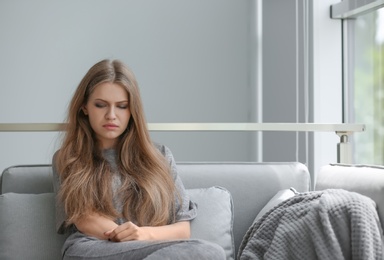 Photo of Depressed young woman sitting on sofa at home