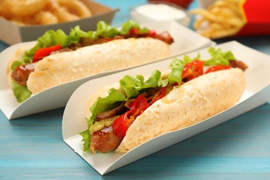 Photo of Tasty hot dogs served on light blue wooden table, closeup. Fast food