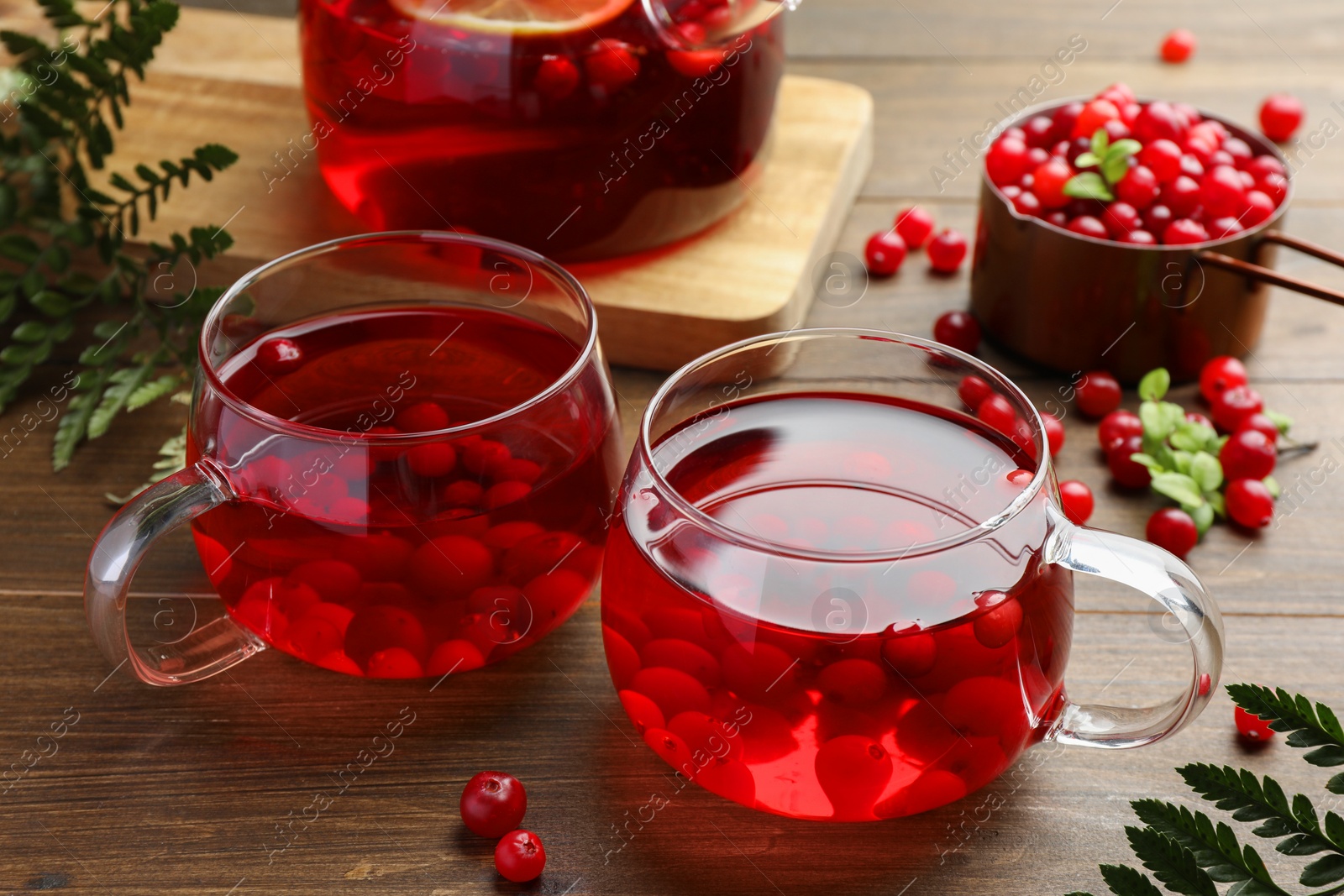 Photo of Tasty hot cranberry tea in glasses and fresh berries on wooden table