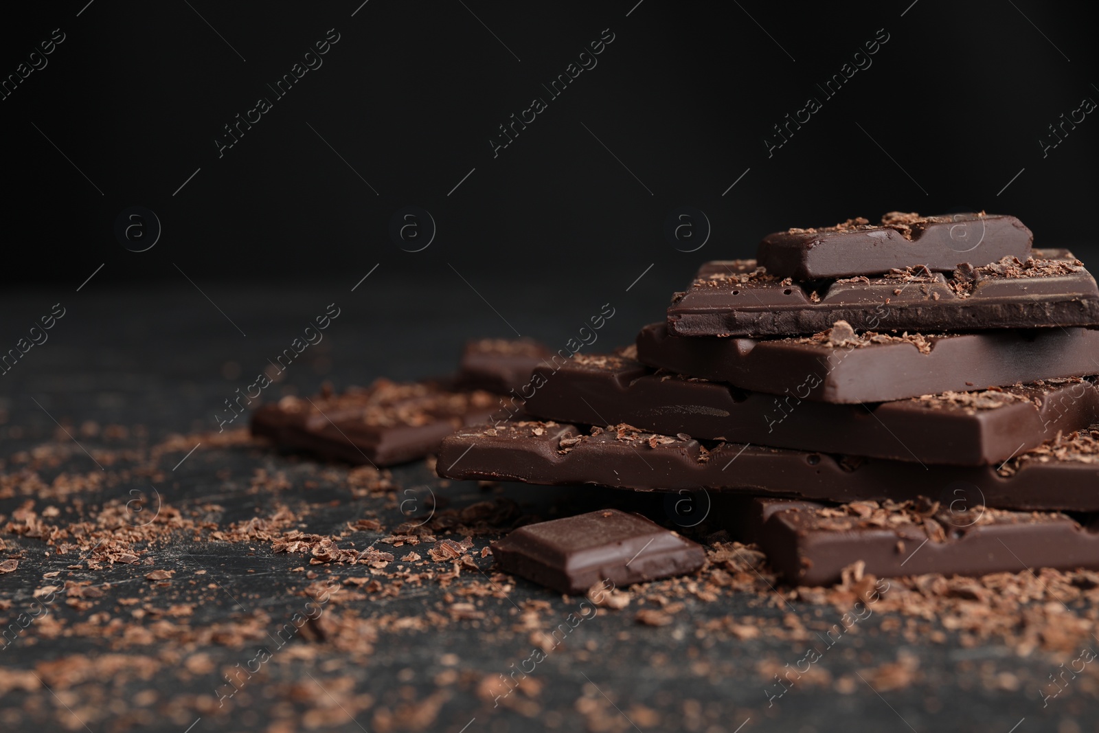 Photo of Pieces and shavings of tasty chocolate on dark table, closeup. Space for text