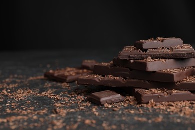 Photo of Pieces and shavings of tasty chocolate on dark table, closeup. Space for text