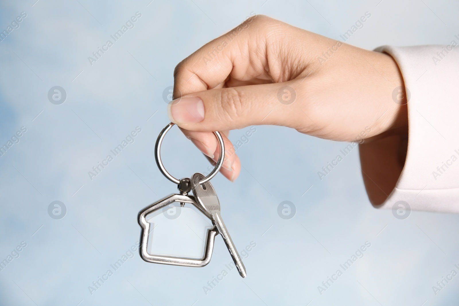 Photo of Woman holding house key with trinket on color background, closeup