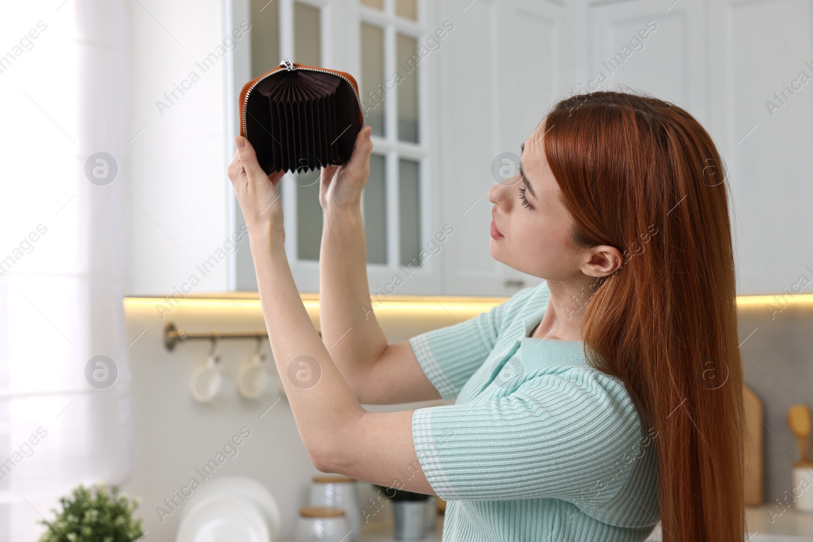 Photo of Upset woman with empty wallet at home