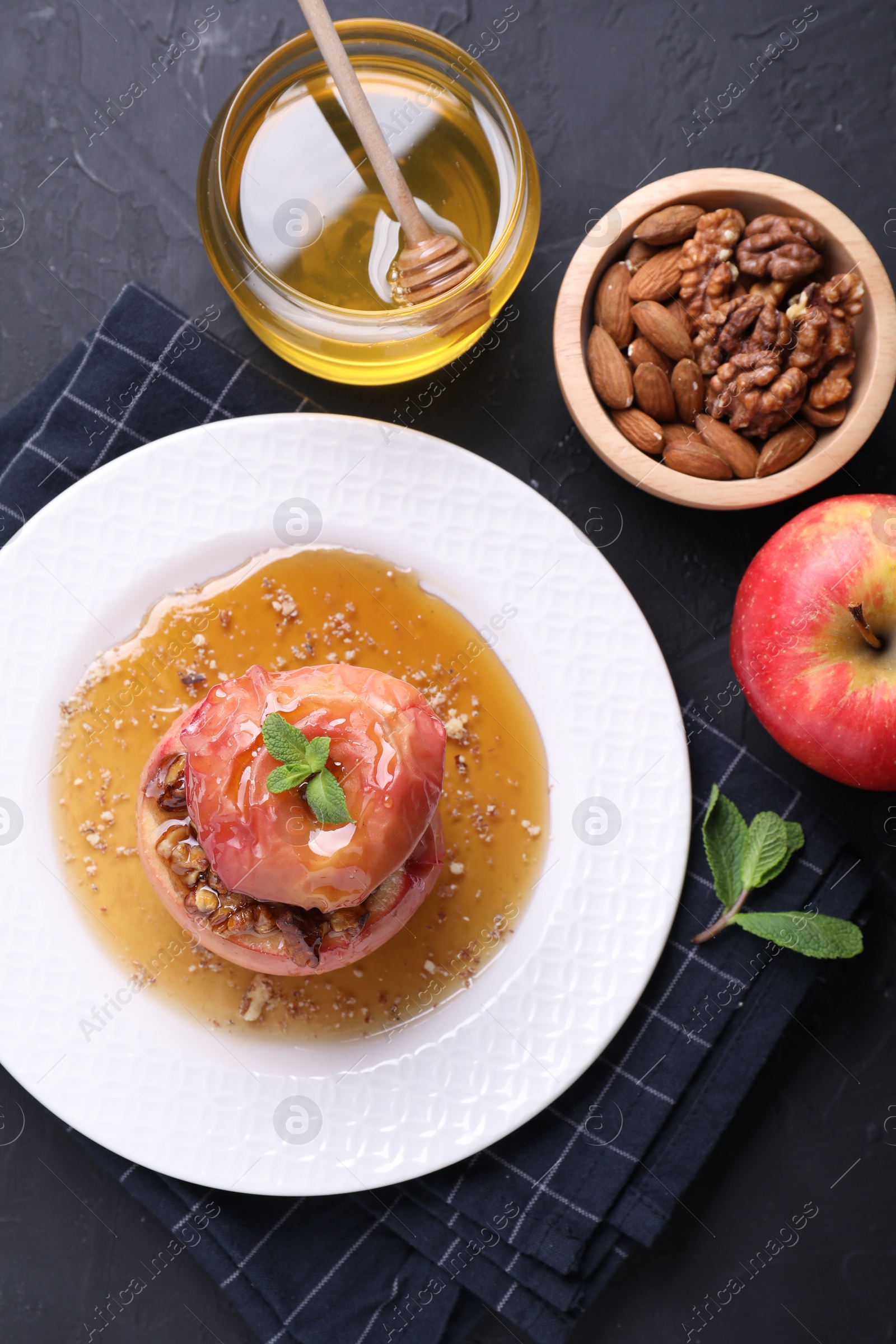 Photo of Tasty baked apple with nuts, honey and mint on gray textured table, flat lay