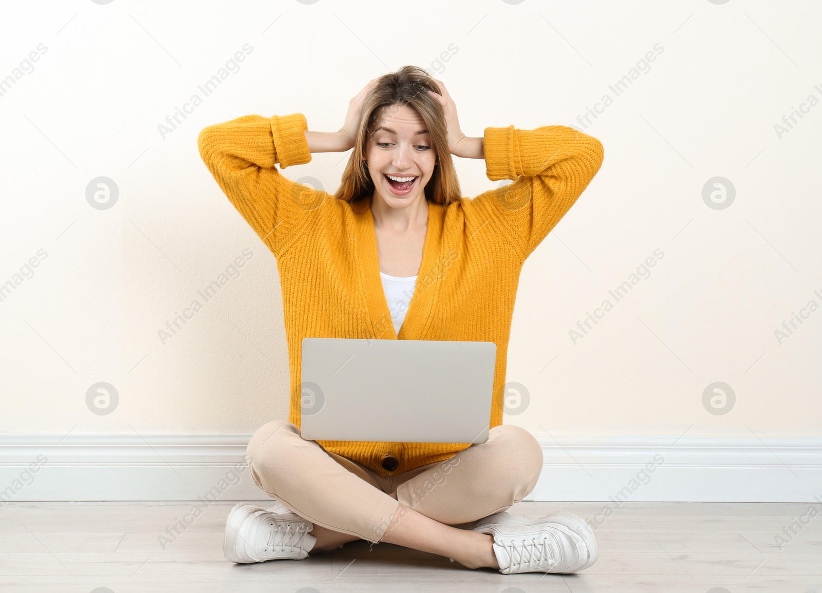 Photo of Surprised young woman with laptop sitting on floor near light wall indoors