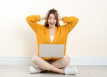 Photo of Surprised young woman with laptop sitting on floor near light wall indoors