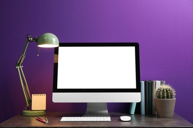 Photo of Comfortable workplace with modern computer and cactus on table near purple wall. Space for design