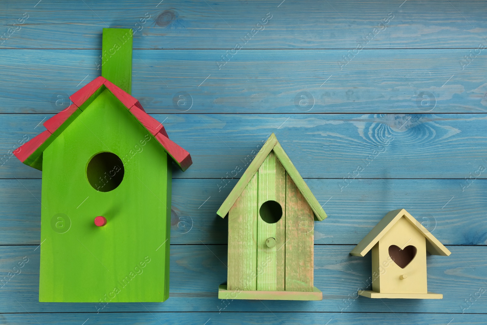 Photo of Three different bird houses on light blue wooden background