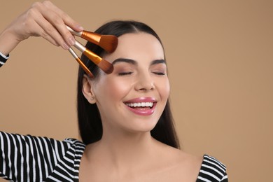 Happy woman with different makeup brushes on light brown background