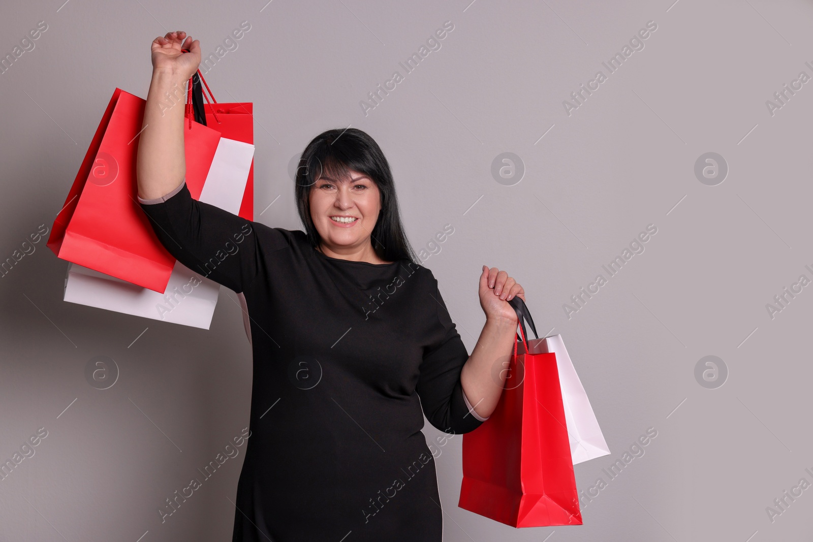 Photo of Beautiful overweight mature woman with shopping bags on light grey background. Space for text