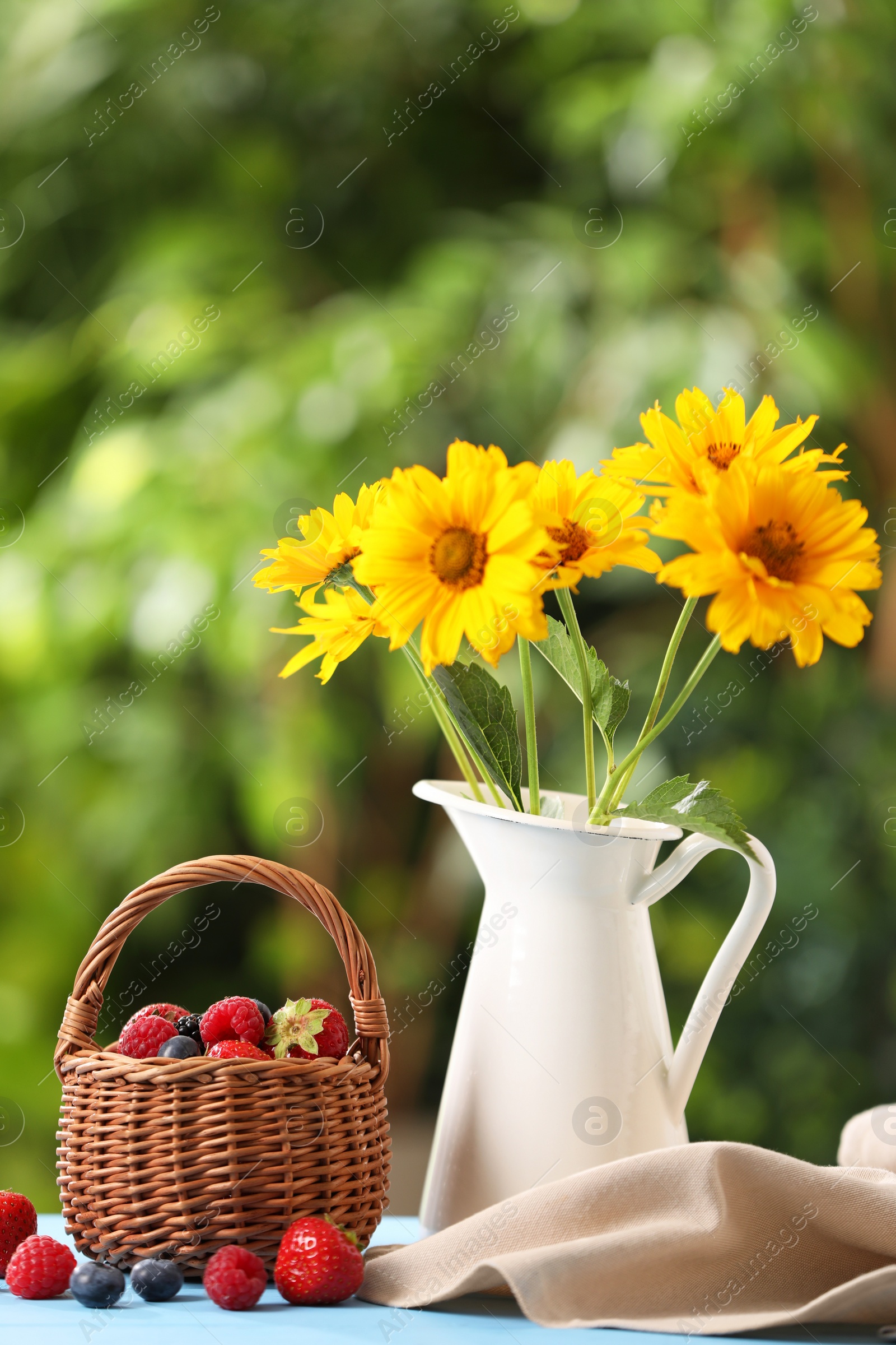 Photo of Wicker basket with different fresh ripe berries and beautiful flowers on light blue table outdoors