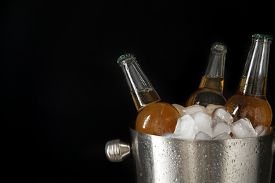 Photo of Metal bucket with bottles of beer and ice cubes on black background. Space for text