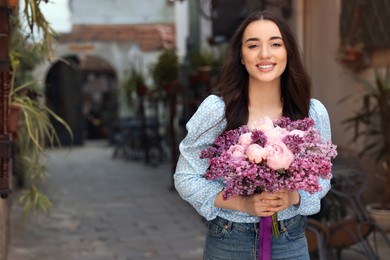 Beautiful woman with bouquet of spring flowers on city street, space for text