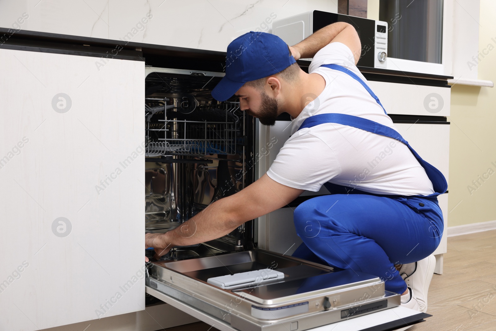 Photo of Serviceman repairing and examining dishwasher in kitchen