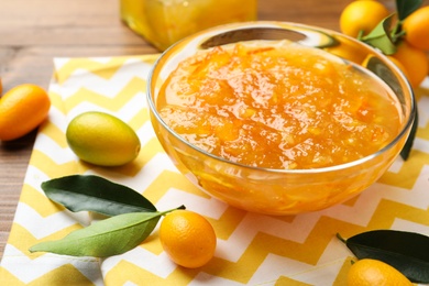 Delicious kumquat jam in bowl and fresh fruits on table, space for text