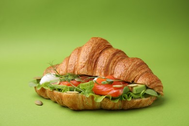 Photo of Tasty croissant with salmon, avocado, mozzarella and lettuce on green background, closeup