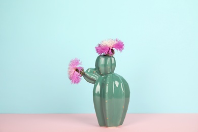 Photo of Trendy cactus shaped ceramic vase with flowers on table against color background