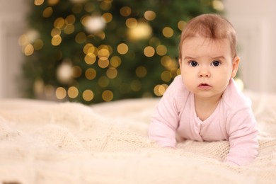 Portrait of cute little baby on knitted blanket against blurred festive lights, space for text. Winter holiday