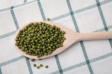 Photo of Wooden spoon with mung beans on kitchen towel, top view