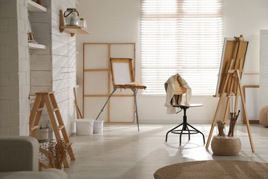 Photo of Modern studio interior with artist's workplace and foldable wooden easel near large window