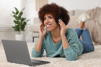 Beautiful young woman in headphones using laptop in room