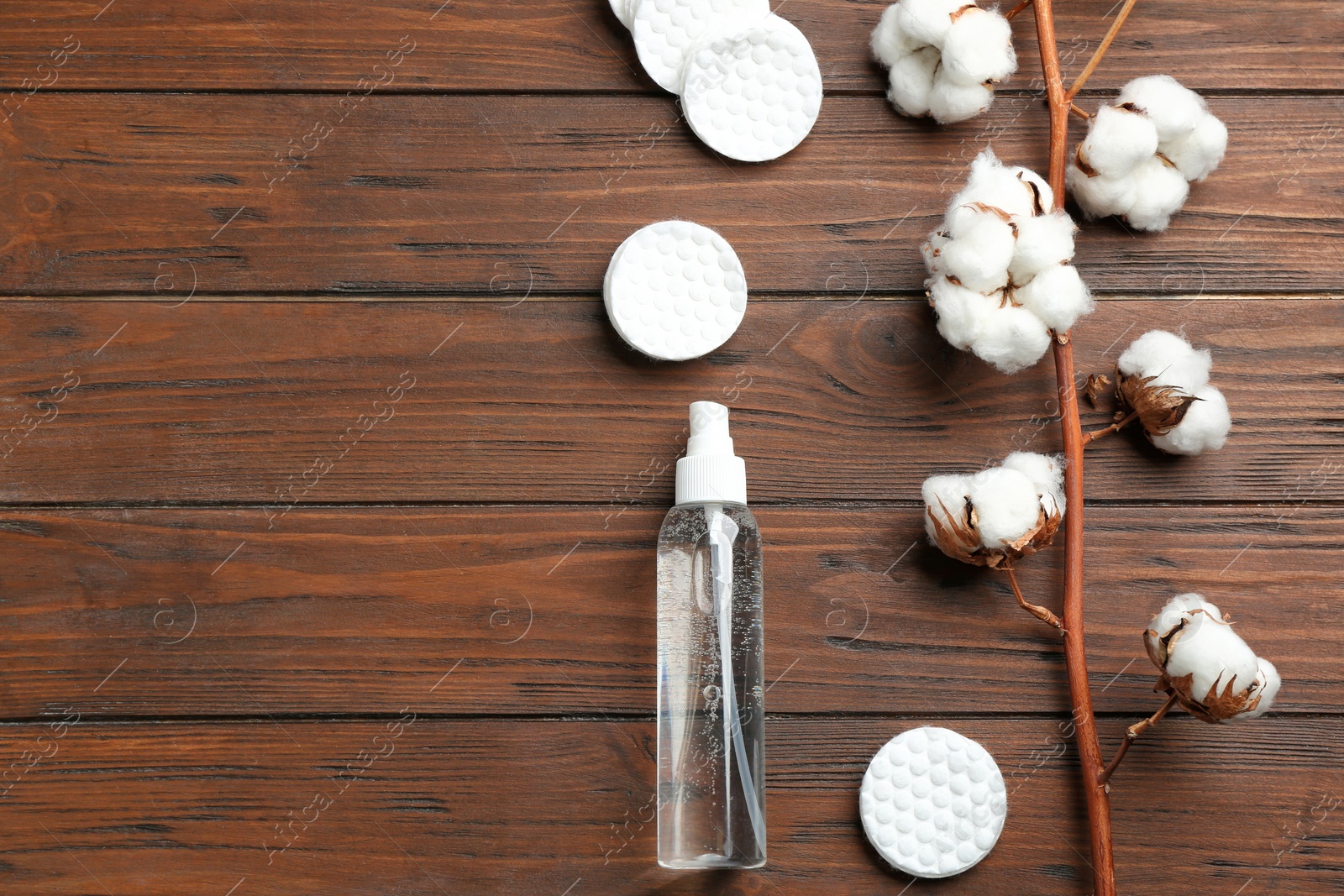 Photo of Flat lay composition with cotton pads, flowers and bottle of cosmetic product on wooden background. Space for text